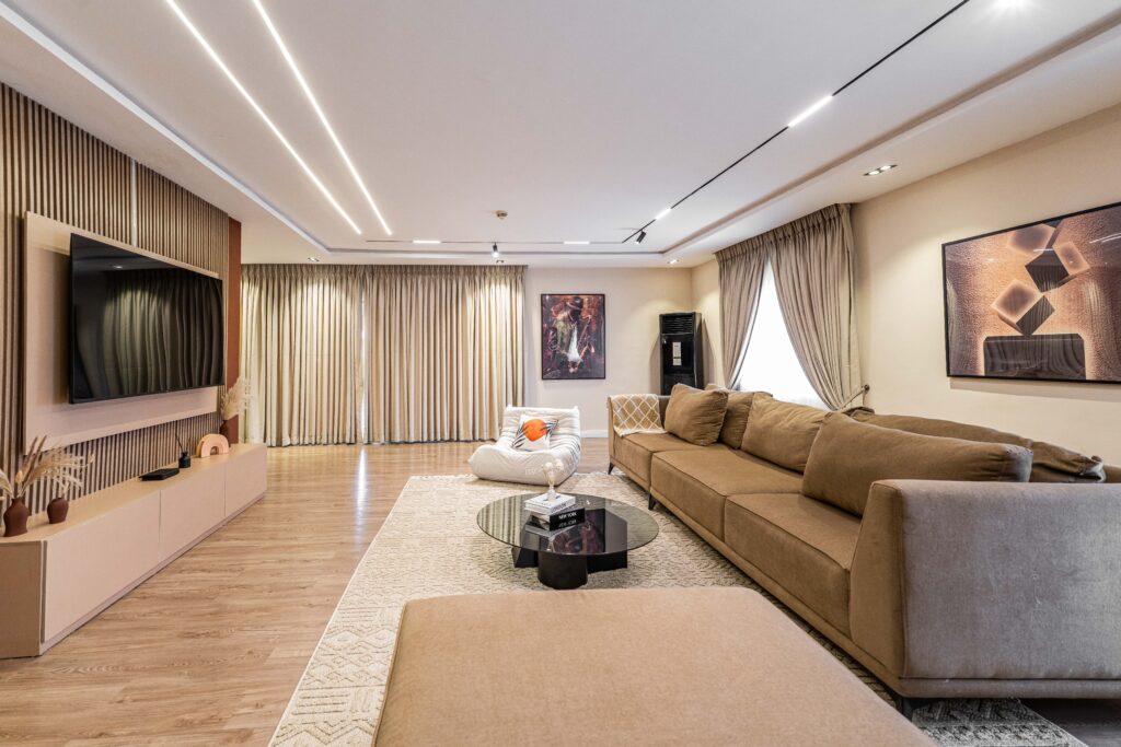 The Ormonde penthouse living room at George Residence, Banana Island — recessed lighting, wood-slat feature wall and taupe seating